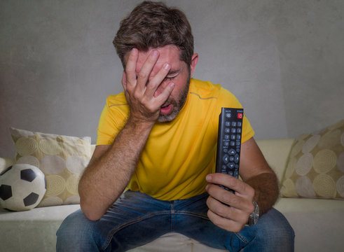 dejected and frustrated man watching European football game on TV sitting at living room couch alone feeling sad and unhappy with his team losing