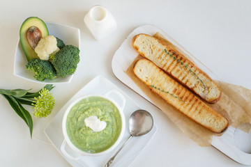 a bowl with vegetables puree on a white background. large white bowl with vegetable green cream soup of broccoli, zucchini, green peas on white background, top view