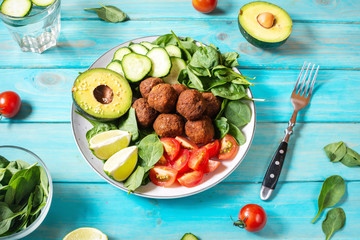 Salad with avocado, falafel, cucumber, cherry tomato and spinach on blue wood background.