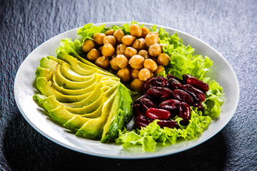 Vegetable salad with chickpea, avocado and red beans in bowl on black stone