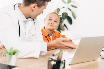 pediatrist in white coat and child using laptop in clinic