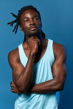 strong muscular dancer making up a performance, movements, repper thinking about new words for song, singer creating a song. close up portrait, isolated blue background, studio shot