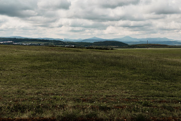 Dramatic landscape.  Green field, mountains and teal thunderclouds.