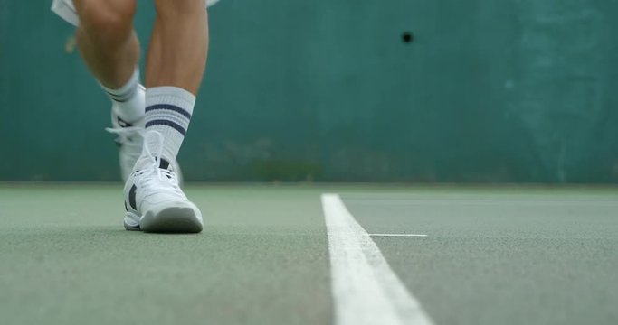 Close up of a tennis player running along the baseline to play a shot in slow motion.