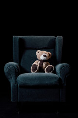 gray soft armchair with plush teddy bear isolated on black