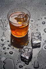 glass of whiskey with ice on a wet surface