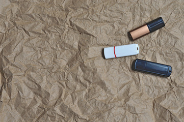Three usb flash drives, white, black and bronze are in different positions on crumpled textured...