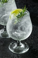 Gin and Tonic Alcohol drink with Lime, Rosemary and ice on rustic black table