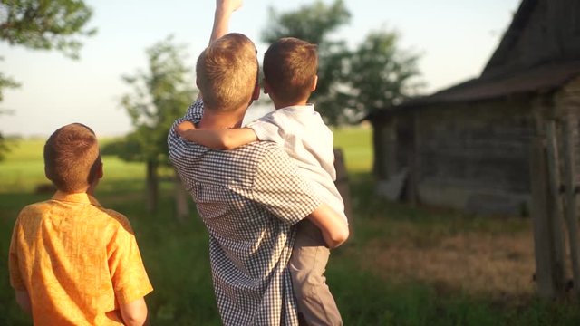 Three brothers hugging each other. Three little boys looking up at the sky. Brothers walk. Three children resting in the village. Three boys of different height stand next to each other.