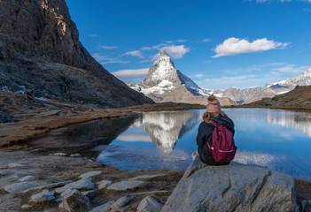 A female hiker looks across lake to the Matterhorn peak in Switzerland.