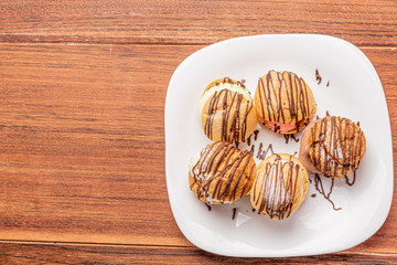 Profiteroles with ice cream and chocolate. Eclairs with black chocolate on wooden background. Traditional French dessert.