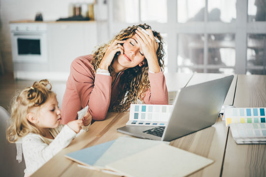 Business Mom Working At Laptop While Talking On Mobile Phone In Overwork. Lifestyle Of Modern Business Mom. Girl Feeling Sad. Business, Motherhood, Multitasking And Family Concept.