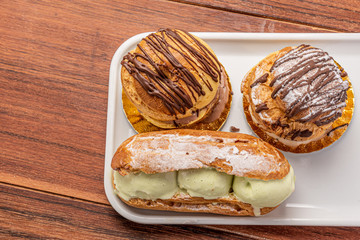 Profiteroles with ice cream and chocolate. Eclairs with black chocolate on wooden background. Traditional French dessert.