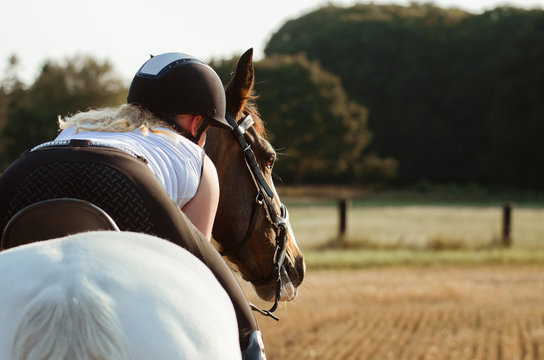 Reiterin liegt auf dem Hals ihres Pferdes auf einem Stoppelfeld 