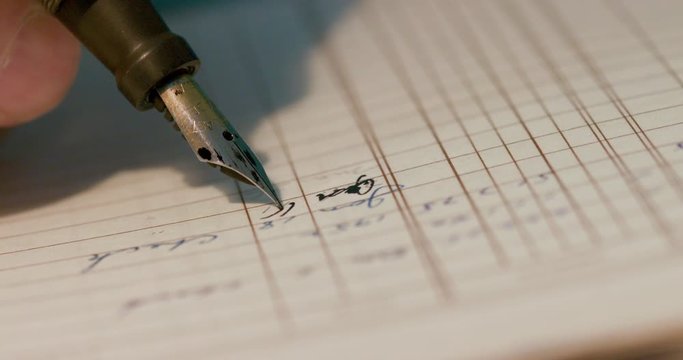 Extreme close up of the tip of an old style fountain ink pen being used to make hand written entries in a ledger.