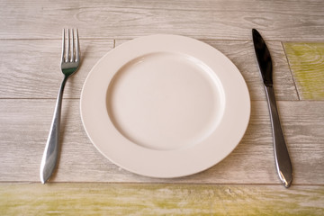 Empty white dish on the wood table with cutlery. 