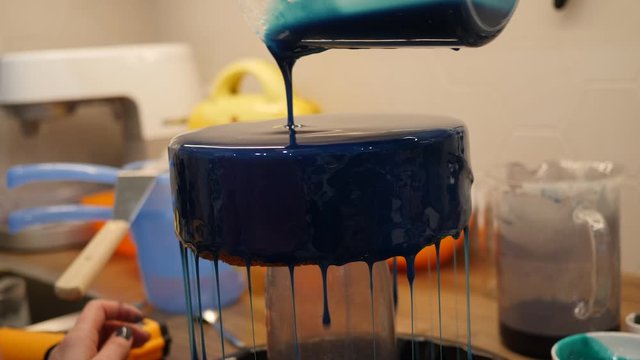 Pouring indigo blue icing on a sweet cake. Making delicious dessert on a kitchen