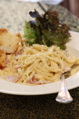Pasta carbonara with bread, ham and cheese on white plate.