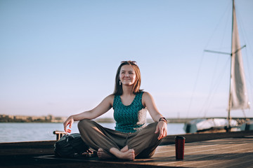 A young woman is sitting on the pier by the yacht