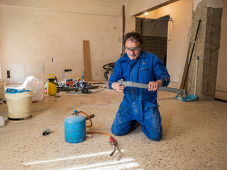 Plumber in a kitchen building site, working with PVC pipes.