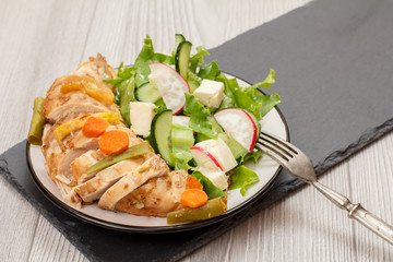 Plate with meat, vegetable salad with cheese, cucumber and radish on stone board.