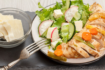 Plate with meat, vegetable salad with cheese, cucumber and radish on stone board.