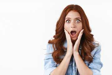Close-up shocked gasping speechless young redhead woman in denim jacket, cup face in hands, open mouth astonished, stare camera with awe and amazement, drop jaw from news, white background - obrazy, fototapety, plakaty