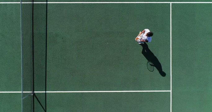 A mixed race tennis player runs backwards on court, smashes a volley and celebrates.