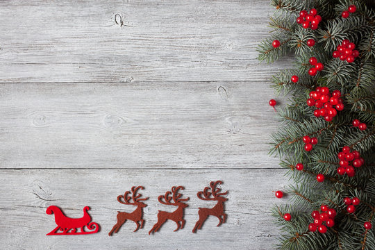 Christmas wooden background with fir branches, red berries and decor deer, sleigh