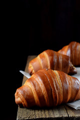 Golden croissants of yeast dough on the edge of the wooden table against black background