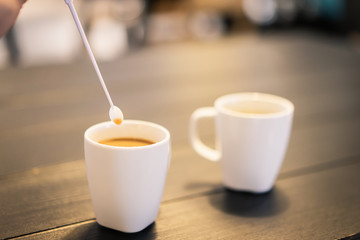 Lady hand holding coffee spoon and stirring hot coffee on wooden table.