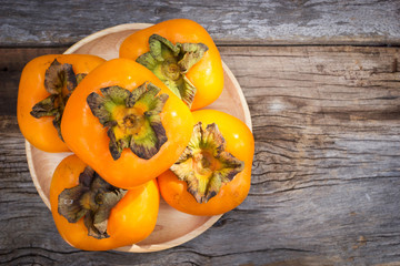 Persimmon on wood plate, wooden table. Tropical fruit. Top view with copy space.