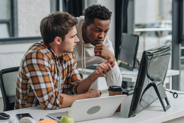 serious programmer gesturing while looking at computer monitor together with african american...