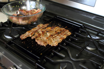 Korean style BBQ shortribs, known as Kalbi, on a cast iron grill in a home kitchen.