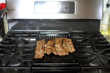 Korean style BBQ shortribs, known as Kalbi, on a cast iron grill in a home kitchen.