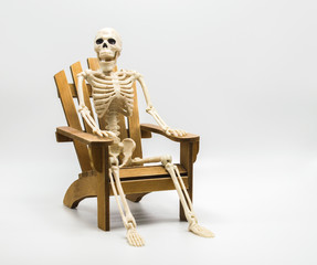 a whimsical Halloween skeleton sitting in a wooden Adirondack chair isolated on white