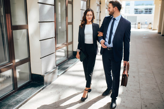 good looking smart man holding a briefcase and having a talk with beautiful female colleague, full length photo.
