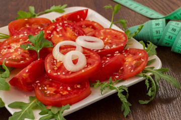 Sliced tomatoes sprinkled with sesame seeds. Arugula leaves. Measuring tape. Low calorie diet concept.