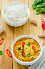 Spicy chicken breast in yellow curry sauce with garlic and chili  pepper with boiled rice in a bowl on a dark wooden background.