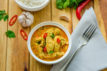 Spicy chicken breast in yellow curry sauce with garlic and chili  pepper with boiled rice in a bowl on a dark wooden background.