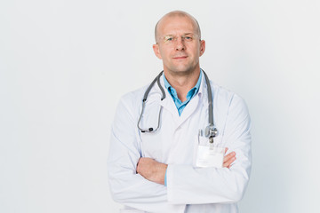 Young successful cross-armed doctor with stethoscope on neck standing by wall