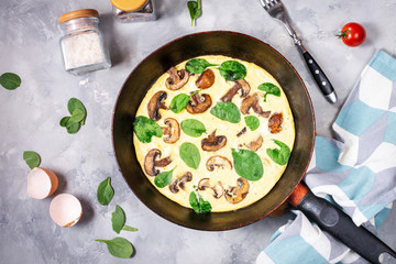 Omelette with mushrooms and spinach in iron pan on concrete background.