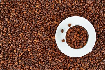 Background of roasted coffee beans. In the foreground is a white coffee Cup with coffee beans.