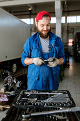Contemporary young worker of car repair service standing by motor of automobile