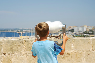Unidentifiable blond child looks through the binoculars at the sea from Gallipoli castle. Apulia,...