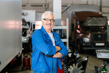 Happy mature cross-armed technician of car maintenance service