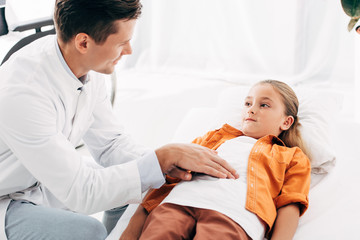 Obraz premium smiling pediatrist in white coat examining child in clinic