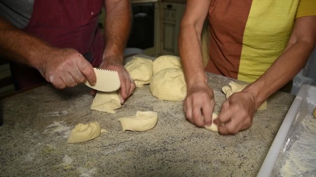 male hands cut dough into pieces to sculpt Italian panzerotti pies, near to female hands roll dough balls on a table. Cooking Panzerotti in Puglia, Salento, Italy