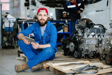 Fototapeta na wymiar Young bearded worker of machine repair service holding touchpad