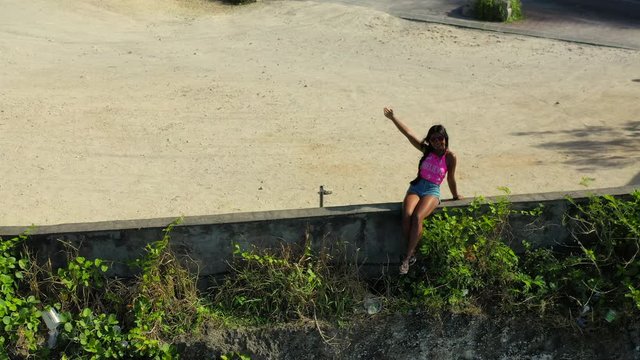 Active lifestyle travel woman sitting on the edge of a cliff and posing on Pantai Pandawa Beach Bali. 4k. Aerial view.